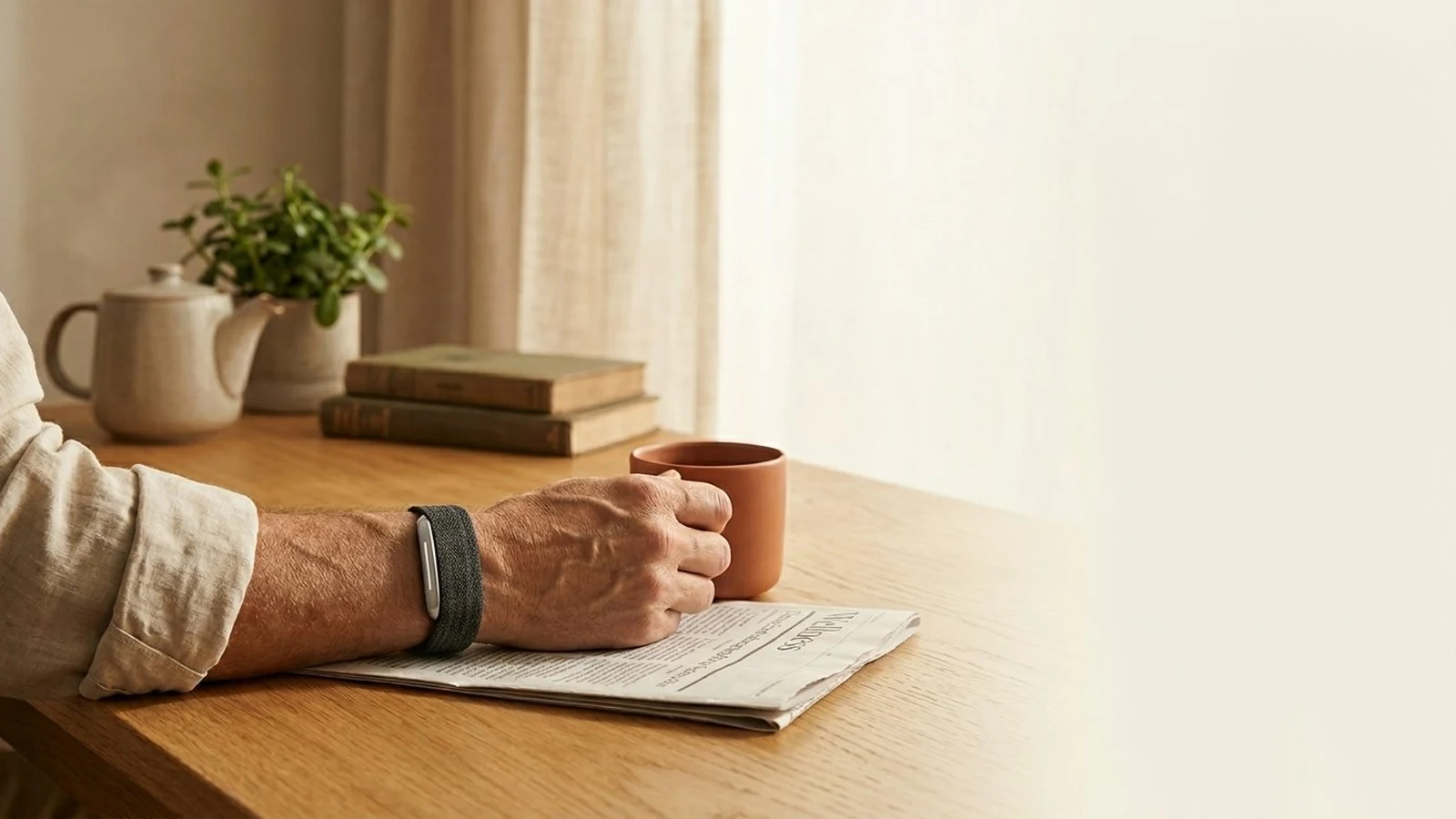 The Hume Band 2.0 worn on the wrist during a quiet morning, coffee and a Wellness newspaper section nearby